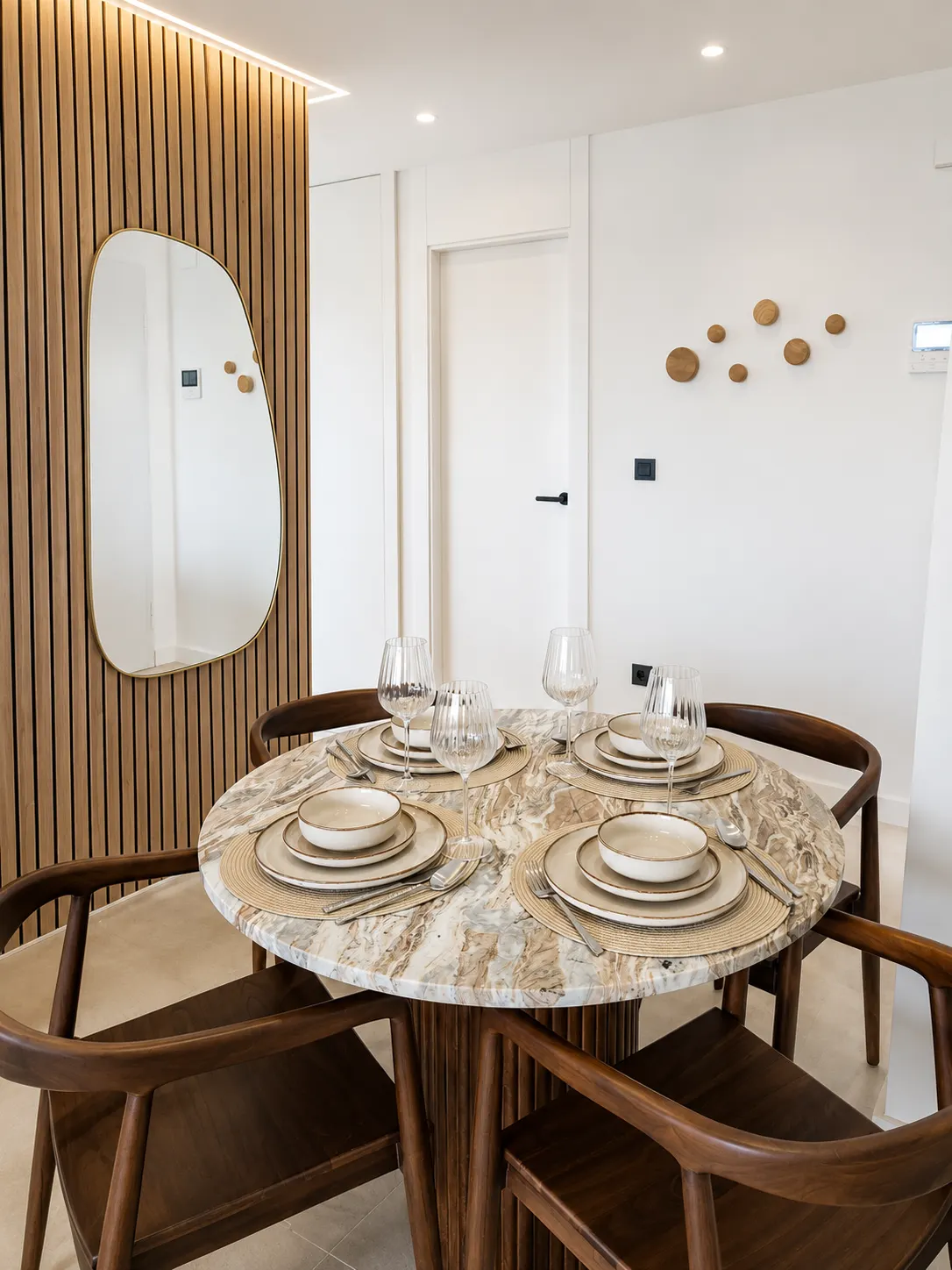 Round table set for four with wooden chairs and a mirror on the slatted wall