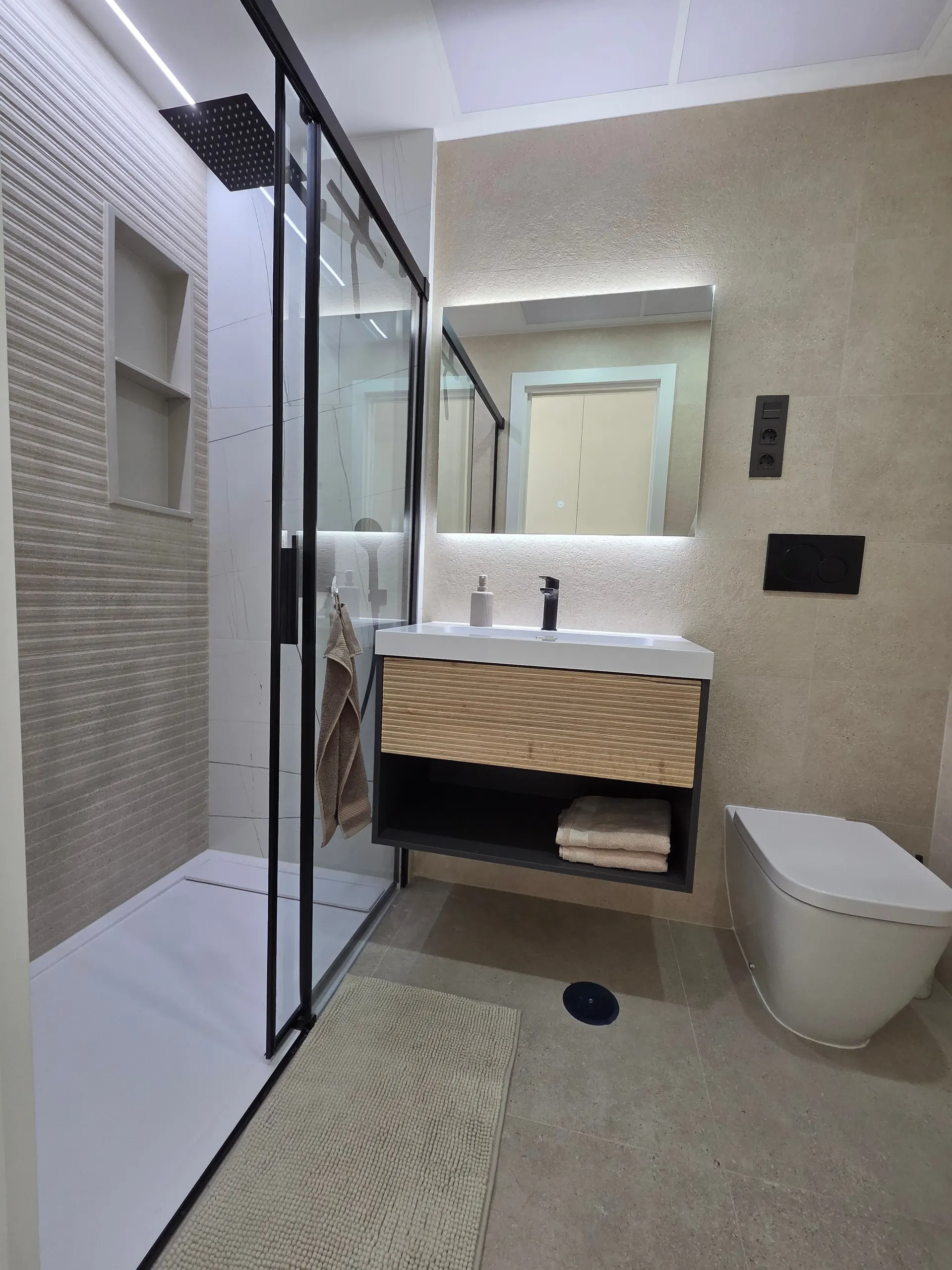 Bathroom with a walk-in shower, a backlit mirror and a wooden vanity